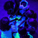 Grupo de niños experimentando con figuras fluorescentes bajo luz ultravioleta.